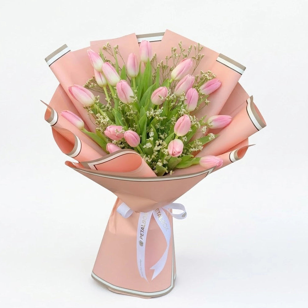 Bouquet of 20 pink tulips wrapped in soft peach paper with green leaves and white ribbon
