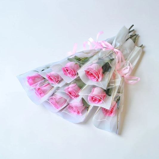 A bunch of 10 Pink roses wrapped in clear plastic with ribbons on a white background
