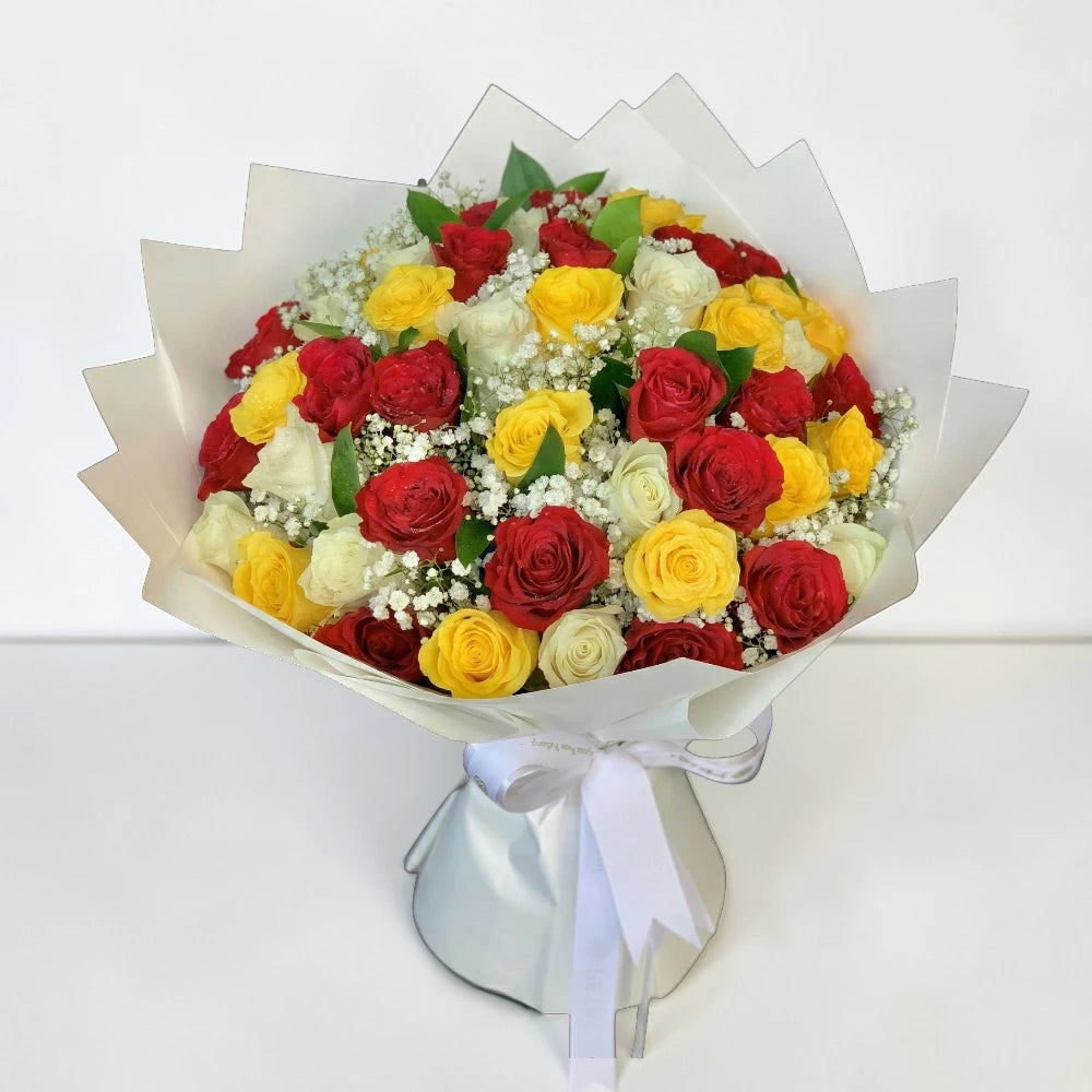 Bouquet of red, yellow, and white roses with a white ribbon on a light gray background