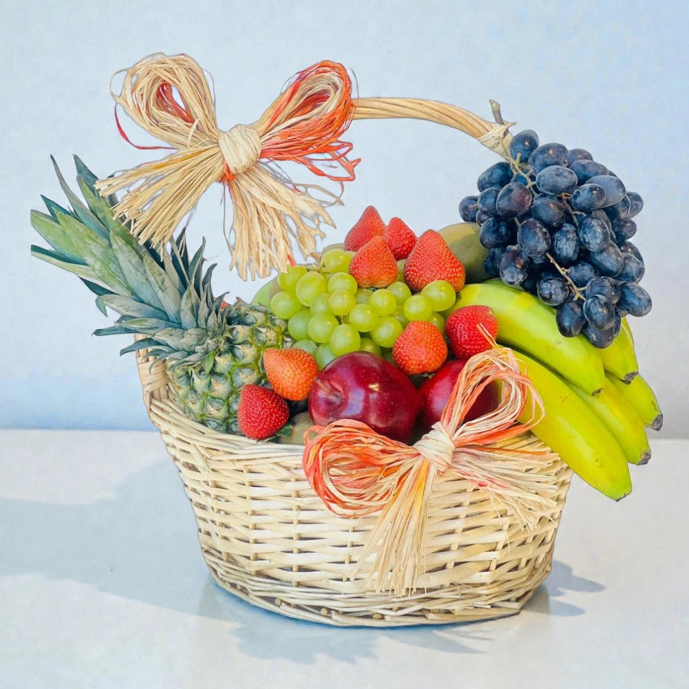 Large woven basket filled with mixed fresh fruits including grapes, pineapple, bananas, apples, and strawberries