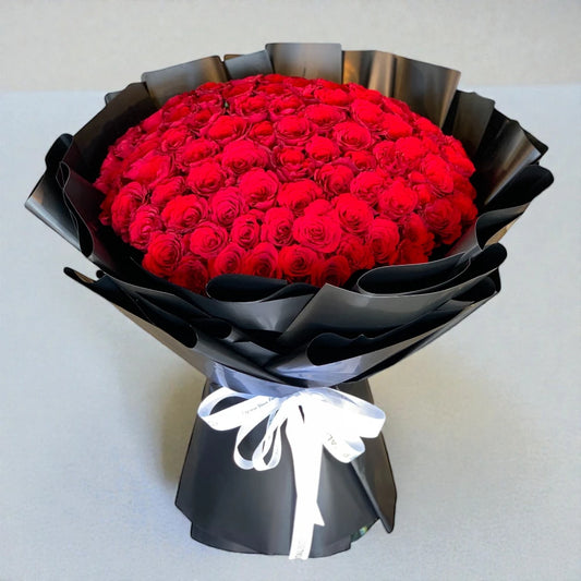 Bouquet of red roses wrapped in black paper with a white ribbon on a light gray background