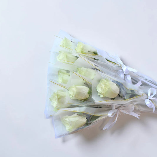 Bouquet of white tulips wrapped in cellophane with a white ribbon on a light background