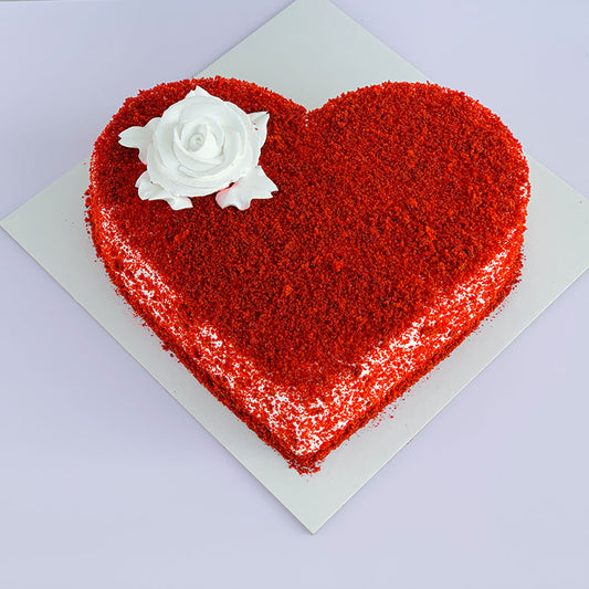 Heart-shaped red velvet cake with white frosting and decorative white rose on top