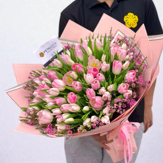 Person holding a bouquet of pink tulips with a visible brand label on a light gray background