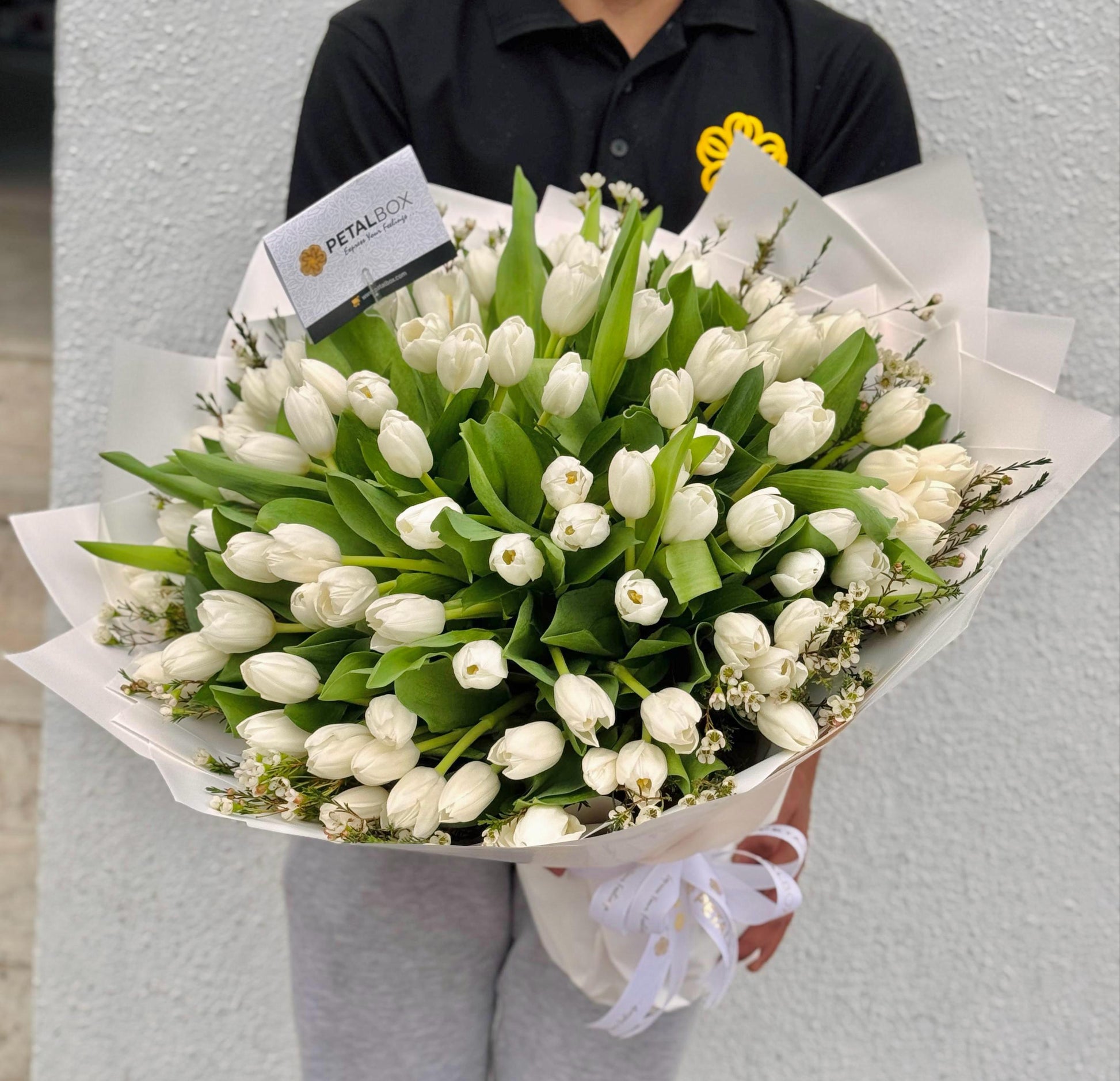 Bouquet of white tulips held by a person with a visible brand label.