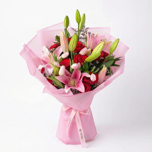 A hand-tied bouquet of pink Oriental lilies, red roses, and soft pink tulips wrapped in blush tissue, available for flower delivery in Kuwait