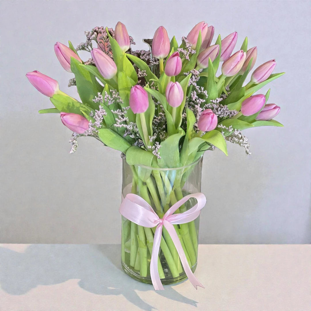 Bouquet of pink tulips in a clear vase with a pink ribbon on a light background