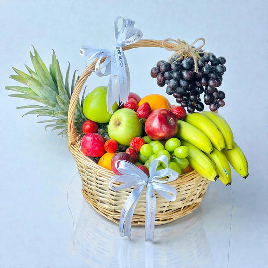Large woven basket filled with fresh pineapple, apples, bananas, grapes, oranges, and strawberries with ribbon detail