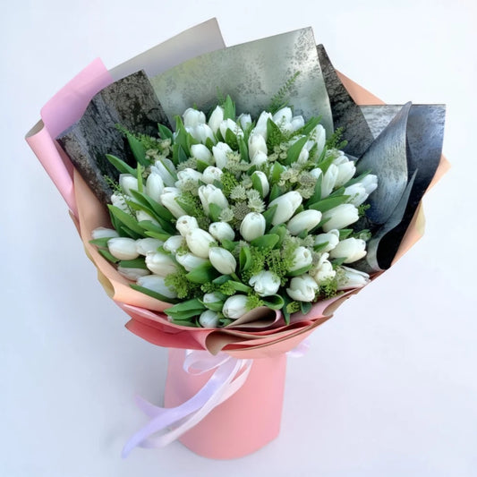 Bouquet of white tulips and greenery wrapped in pink paper 
