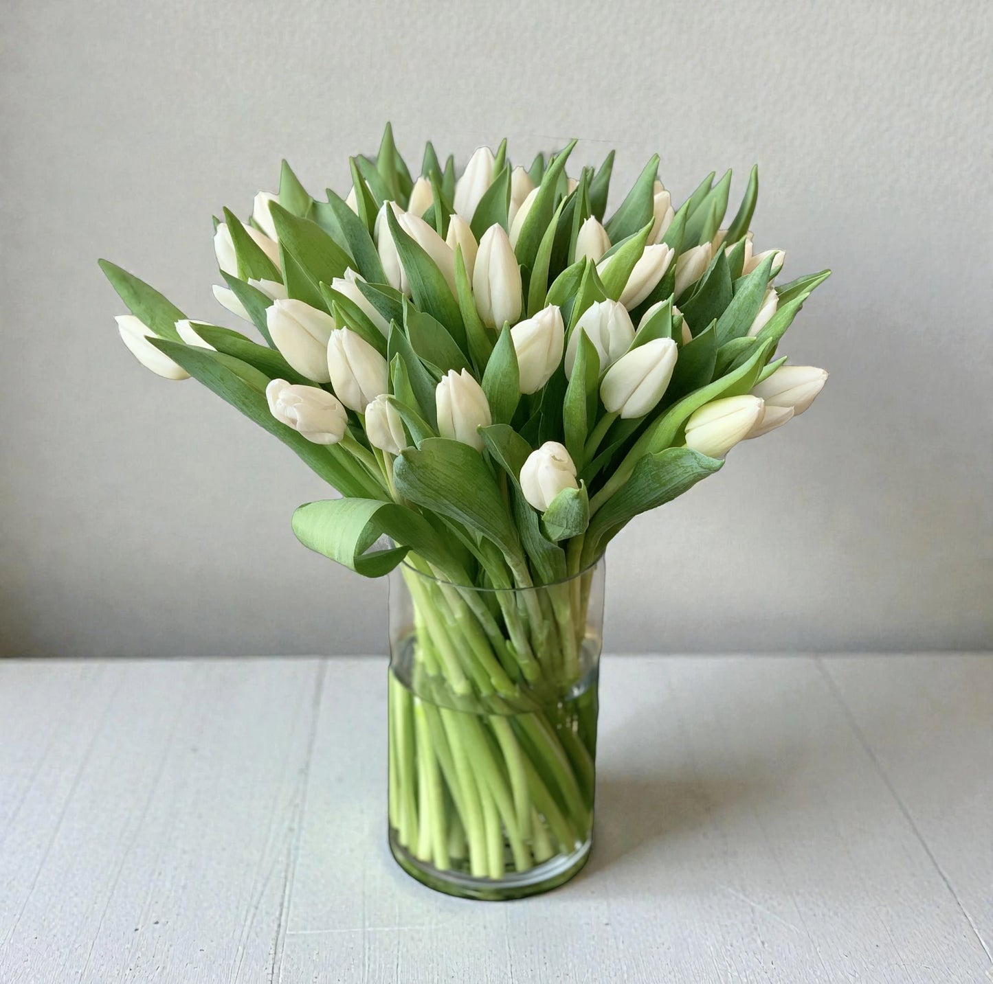 Bouquet of white tulips in a clear vase on a light surface with a neutral background
