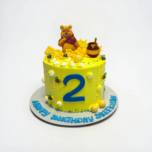 Yellow birthday cake with number 2 and Winnie the Pooh decoration on a white background